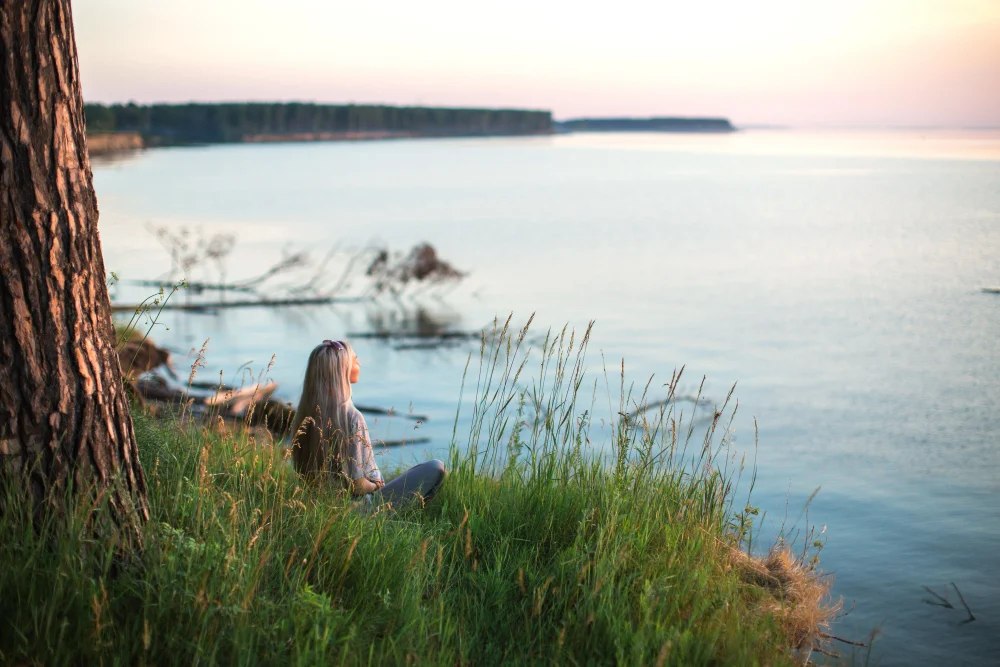 A woman sitting alone by a quiet lakeside at sunset